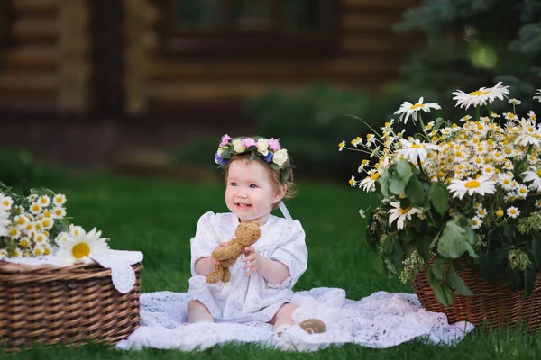 Malá holčička objetí medvěda na trávníku s květinami — Stock fotografie