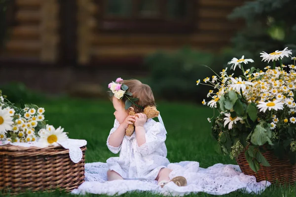 Mała dziewczynka uścisków niedźwiedzia na trawniku z kwiatami — Zdjęcie stockowe