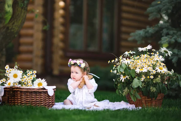 Mała dziewczynka uścisków niedźwiedzia na trawniku z kwiatami — Zdjęcie stockowe