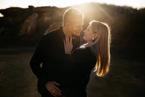 Retrato vista lateral de dos jóvenes amantes besándose al atardecer sobre fondo barranco. Pareja en ropa negra —  Fotos de Stock