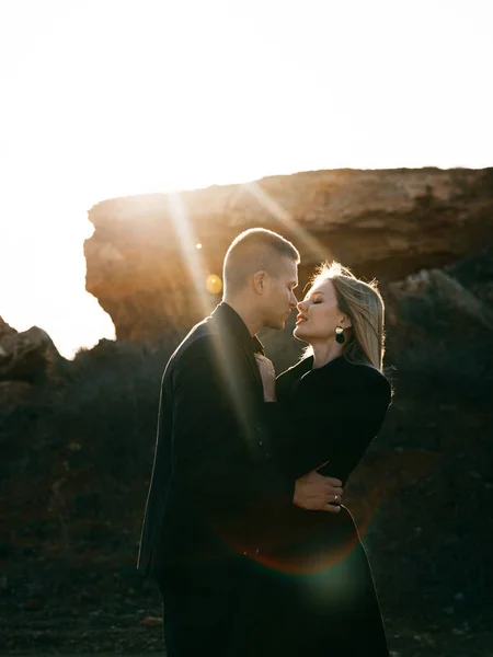 Portrait latéral de deux jeunes amants s'embrassant au coucher du soleil sur fond de ravin. Couple en vêtements noirs Photos De Stock Libres De Droits