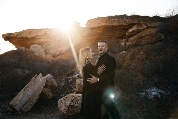 Portrait latéral de deux jeunes amants s'embrassant au coucher du soleil sur fond de ravin. Couple en vêtements noirs Image En Vente