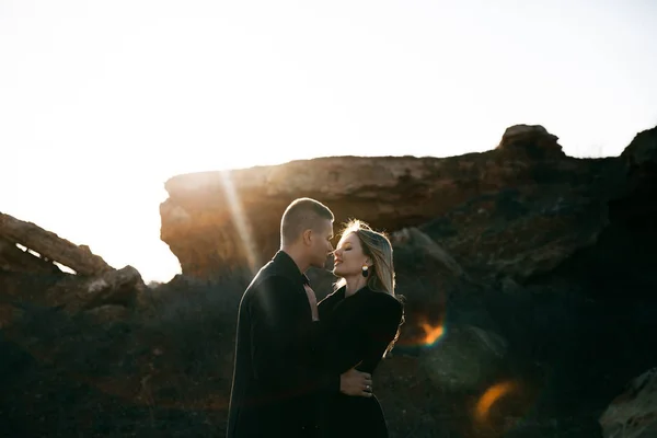 Retrato de vista lateral de dois jovens amantes se beijando ao pôr do sol no fundo ravina. Casal em roupas pretas — Fotografia de Stock