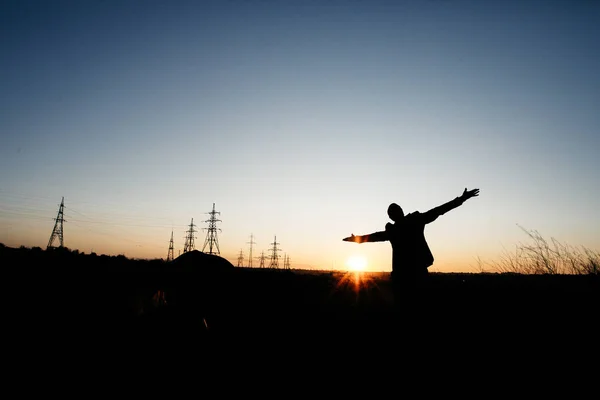 El hombre extiende sus manos sobre el fondo de las líneas eléctricas. Salvar el planeta y la electricidad. Siente la libertad. Energy Distribution Network - Electricity Pylons against Orange and Yellow Sunset (en inglés). Las torres Eiffel —  Fotos de Stock