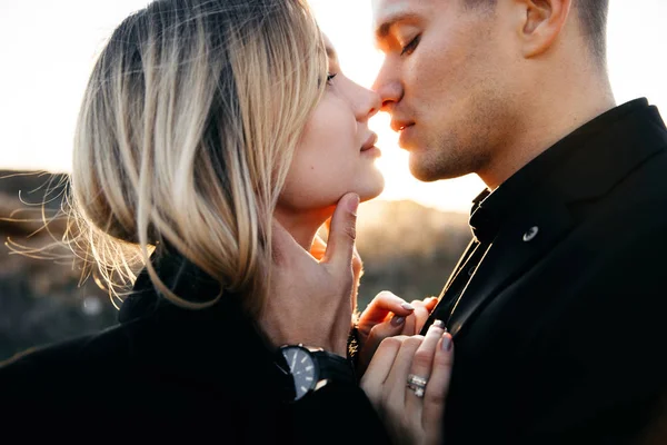 Tampilan samping foto dari dua pecinta muda berciuman saat matahari terbenam. Man lembut menyentuh gadis cantik. Pengantin baru dalam pakaian hitam — Stok Foto