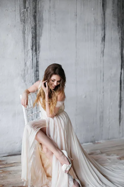 Modemodel in een prachtige beige vloeiende jurk. bruidsschat. Bruidsochtend. In focuse meisjes fragiele benen in een beige jurk en hiel schoenen. — Stockfoto