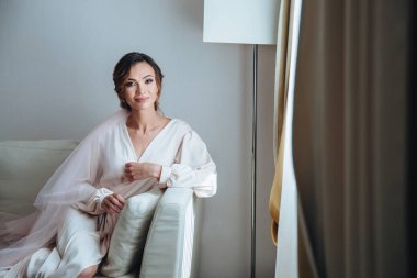 Günaydın gelin, güzel gelin beyaz odadaki kanepede oturmuş düğünü bekliyor. Pencerenin önündeki gelinlikli kız damadı bekliyor.