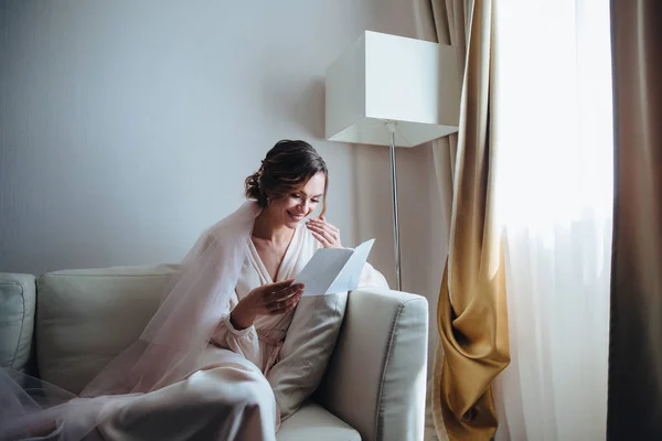 Pagi pengantin, pengantin cantik sedang menunggu untuk pernikahan duduk di sofa di ruang putih. Gadis dengan gaun pengantin di depan jendela sedang menunggu pengantin pria Stok Lukisan  