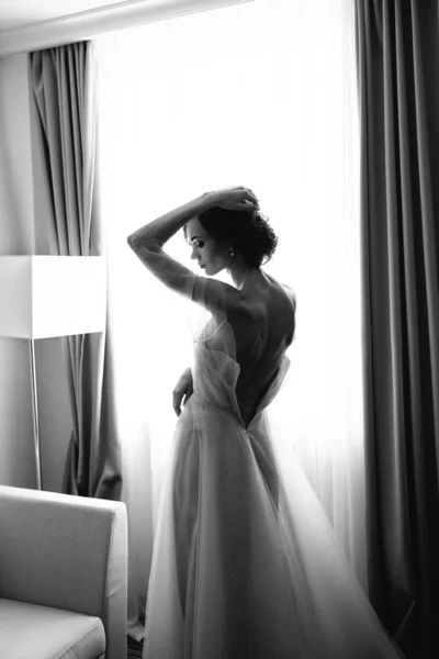 Retrato preto e branco da noiva com vestido aberto das costas no fundo da janela. Belo decote no vestido com sexy costas abertas da noiva — Fotografia de Stock