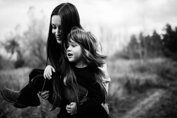 Black and white photo of Young beautiful mom holds son in her arms and smiles on field and forest background. Parenthood — Stock Photo, Image