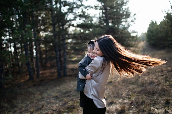 Young beautiful mom turns over daughter in her arms on the forest background. Parenthood. Mom hugs daughter — 스톡 사진