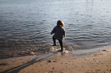 Sonbaharda nehir kıyısında suda koşan bir çocuk. Arkadan bak. Sıcak bir sonbahar günü. İtaatsizlik. Gün batımında nehir kıyısında yalnız bir çocuk. Duygular.