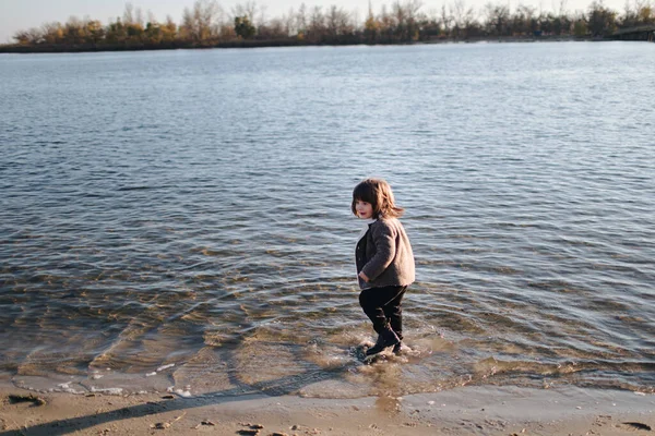 Дитина ходить у річковій воді в темному одязі восени. Теплий осінній день. непокора. Самотня дитина на березі річки на заході сонця. Емоції . — стокове фото