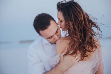 Deniz kıyısındaki çekici yeni evliler. Gelinlerin omuzlarını öpmek. yan ve arka görünüm