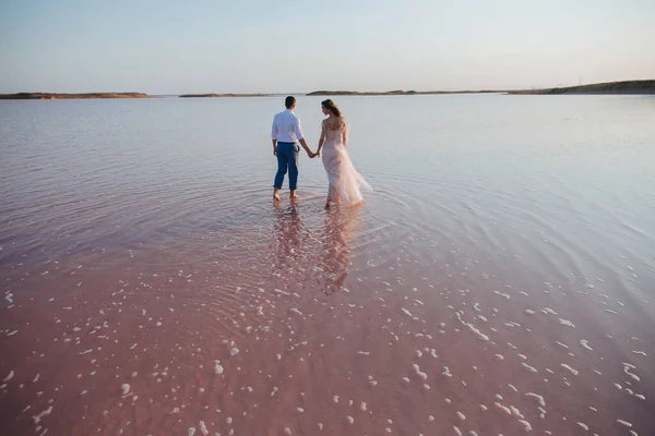 Couple nouvellement marié tenant leurs mains marchant par la mer . Photos De Stock Libres De Droits