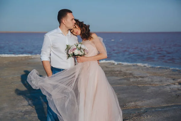 Beautiful newlyweds on the sea shore and gentle groom, hugging the bride. front view. Royalty Free Stock Photos