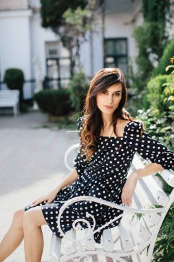 Bahar günü kameraya poz veren benekli siyah elbiseli bir model.