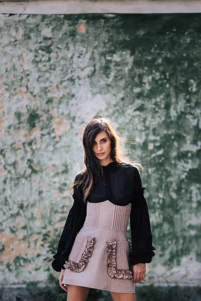 Bonita morena modelo en un vestido de diseñador posando en la cámara en el día de primavera en el fondo de la pared vieja — Foto de Stock