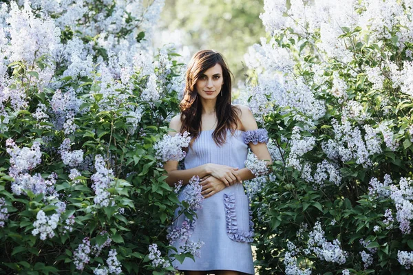 Brünetten Model in einem blauen Designer-Kleid posieren vor der Kamera in fliederfarbenen Blumen an einem Frühlingstag — Stockfoto