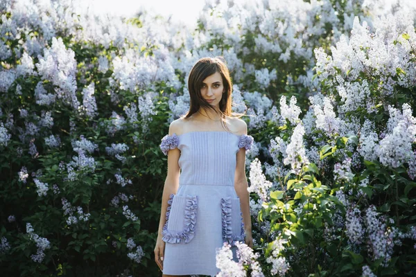 Das Model posiert am Frühlingstag in einem Designer-blauen Kleid in fliederfarbenen Blumen vor der Kamera. Model in fliederfarbenem Kleid und Wind im Haar — Stockfoto