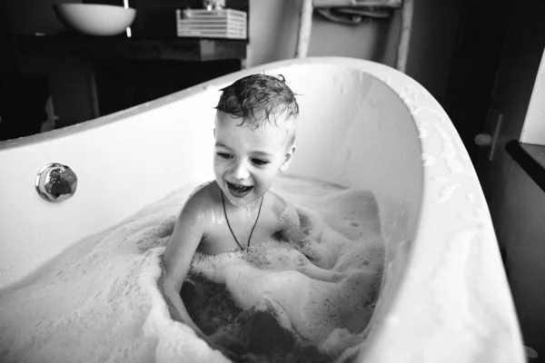 Photo en noir et blanc d'un garçon éclaboussant dans la salle de bain. Vue latérale d'enfants nus jouant dans un bain ovale Images De Stock Libres De Droits