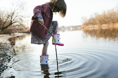 Tekboynuz çizmeli mutlu kız çocuğu baharda su birikintilerinde koşup zıplıyor.