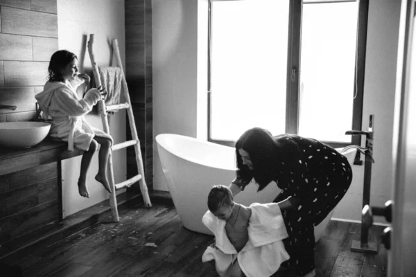 Foto en blanco y negro de mamá limpia a su hijo con una toalla después de tomar un baño y hermana cerca de ellos en un albornoz unicornio blanco . — Foto de Stock