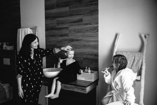 Mom and Two smiling kids brother and sister in unicorn bathrobes brush their teeth after having bath Stockbild