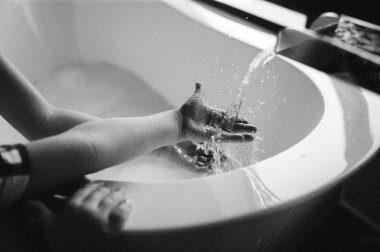 Black and white photo of child having fun and catching a spray of water from faucet