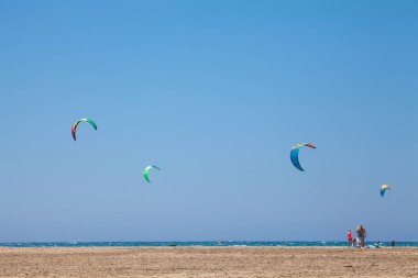 Uçurtma alıştırması yapan insanlar. Prasonisi, Rhodes yarımadasındaki plaj. Deniz kıyısında renkli uçurtmalar. Mavi deniz ve rüzgar sörfü.