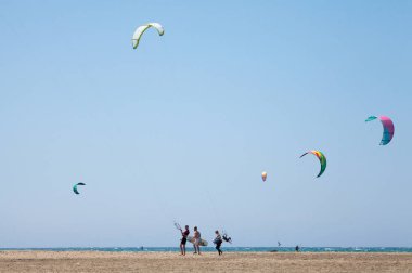 Uçurtma alıştırması yapan insanlar. Prasonisi, Rhodes yarımadasındaki plaj. Deniz kıyısında renkli uçurtmalar. Mavi deniz ve rüzgar sörfü.
