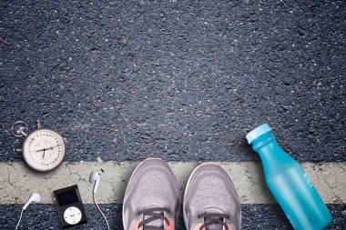 Kadınlar koşu ayakkabıları ve runner ekipmanları asfalt üzerinde. Eğitim zor yüzeylerde. Runner ekipman kronometre ve müzik çalar. Gerekli su şişesi. Arka plan üzerinde asfalt. Zaman çalışan.