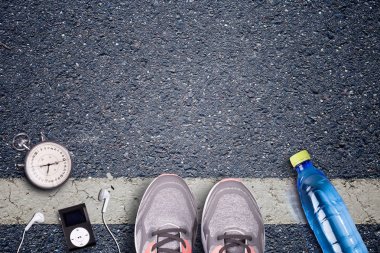 Kadınlar koşu ayakkabıları ve runner ekipmanları asfalt üzerinde. Eğitim zor yüzeylerde. Runner ekipman kronometre ve müzik çalar. Gerekli su şişesi. Arka plan üzerinde asfalt. Zaman çalışan.