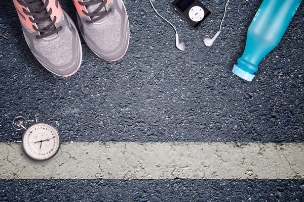 Women Running shoes and runner equipment on asphalt. Training on hard surfaces. Runner Equipment stopwatch and music player. The necessary water bottle. Asphalt on the background. Time to running.