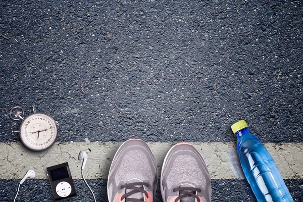 Women Running shoes and runner equipment on asphalt. Training on hard surfaces. Runner Equipment stopwatch and music player. The necessary water bottle. Asphalt on the background. Time to running.