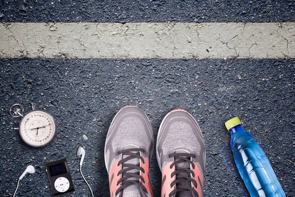 Women Running shoes and runner equipment on asphalt. Training on hard surfaces. Runner Equipment stopwatch and music player. The necessary water bottle. Asphalt on the background. Time to running.