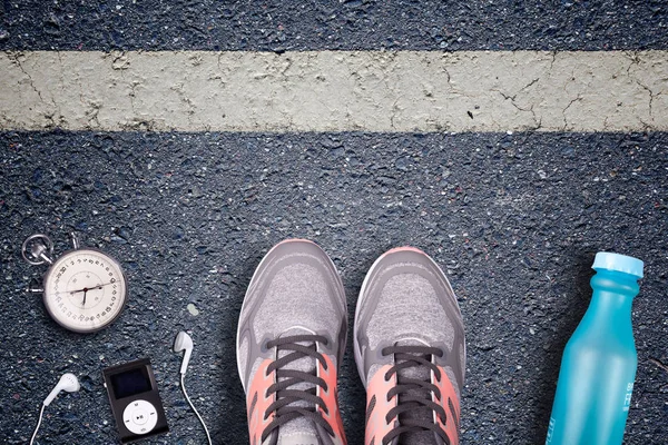 Women Running shoes and runner equipment on asphalt. Training on hard surfaces. Runner Equipment stopwatch and music player. The necessary water bottle. Asphalt on the background. Time to running.