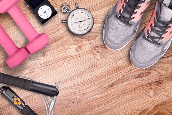 Fitness gym and running equipment. Dumbbells and running shoes, analog stopwatch and music player. Time for fitness and run. Sport accessories for women on the wooden floor.