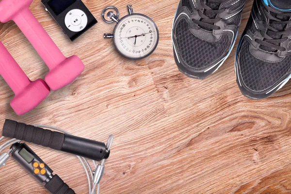 Fitness gym and running equipment. Dumbbells and running shoes, analog stopwatch and music player. Time for fitness and run. Sport accessories on the wooden floor.