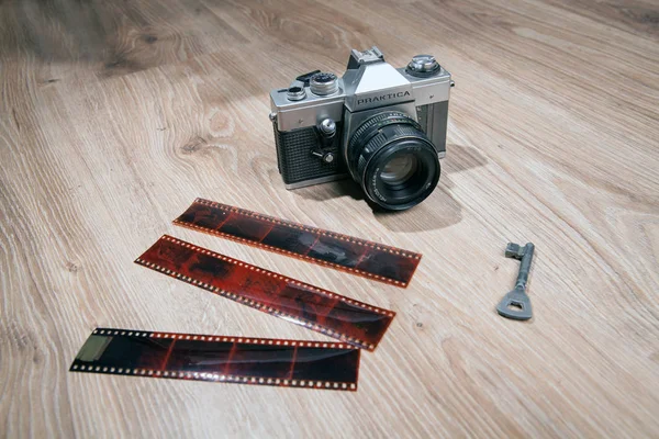 Old analog camera Praktica PLC on a wood background. camera with a short strap. Vintage hipster style. Key on the table.