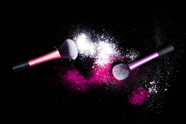 Make-up brushes with colorful powder on black background. White and pink color powder on brushes.