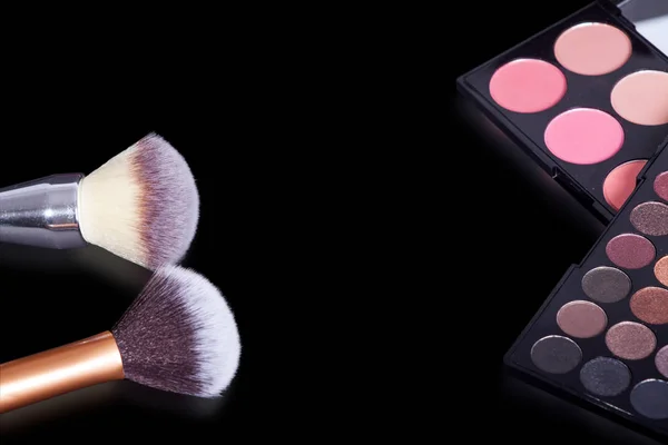 Makeup palette and makeup brush on pure black background. A rich color palette with pink.