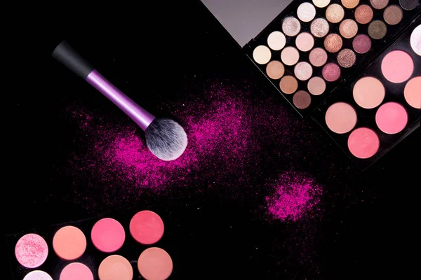 Colorful makeup palette and pink big brush to apply powder. on pure black background. Professional makeup equipment.