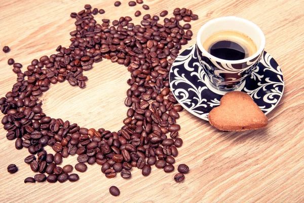 Kalp ahşap masa arka plan üzerinde beyaz kahve çekirdekleri ve Kupası whit espresso ve tatlı kalp kurabiye yapmak. 