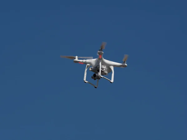 Underneath bottom view of a drone with stabilizer camera flying aerial overhead against a blue sky