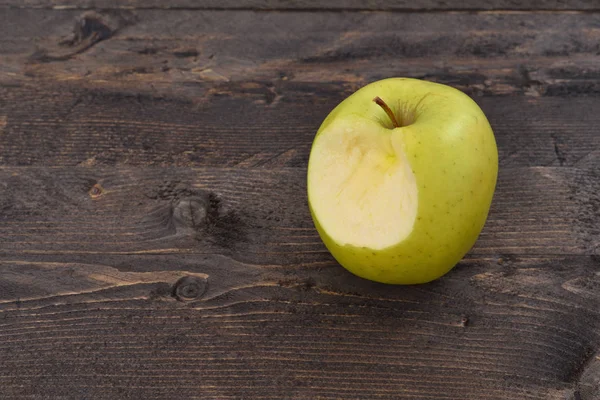 One bitten green apple on a brown wooden desk, top angle view