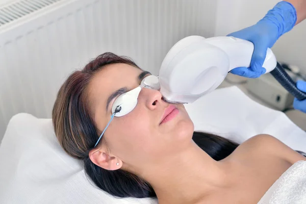 Mooie jonge vrouw liggend op een tafel met protect bril op ogen krijgen een laserbehandeling van de huid — Stockfoto