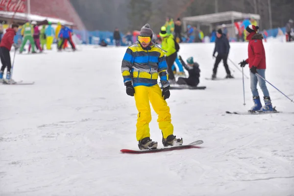 Anak muda di snowboard downhill dengan orang-orang di latar belakang — Stok Foto