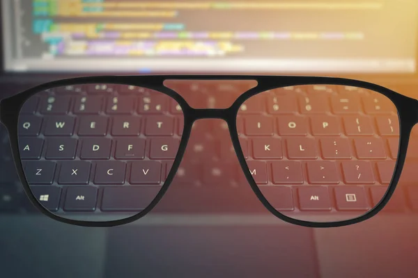 Klares Bild in Brille gegen verschwommene Tastatur mit Codetext auf verschwommenem Bildschirm — Stockfoto