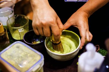 Kadının elinde kullanım bir fırça makinesi kapatın. Çay tozu ve su, birleştirmek için karıştırın ahşap masaüstüne yerleştirdiğiniz